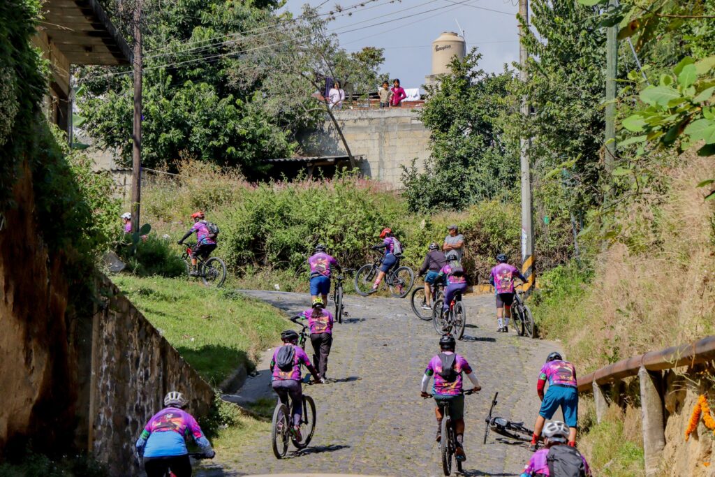 Ciclista de montaña (MTB) disfrutando de un recorrido de turismo de aventura en los senderos rurales de Tochimilco, Puebla, con el volcán Popocatépetl al fondo. Evento organizado por Lambdascore.